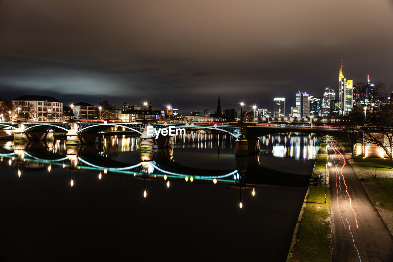 ILLUMINATED BRIDGE OVER RIVER AND BUILDINGS AGAINST SKY