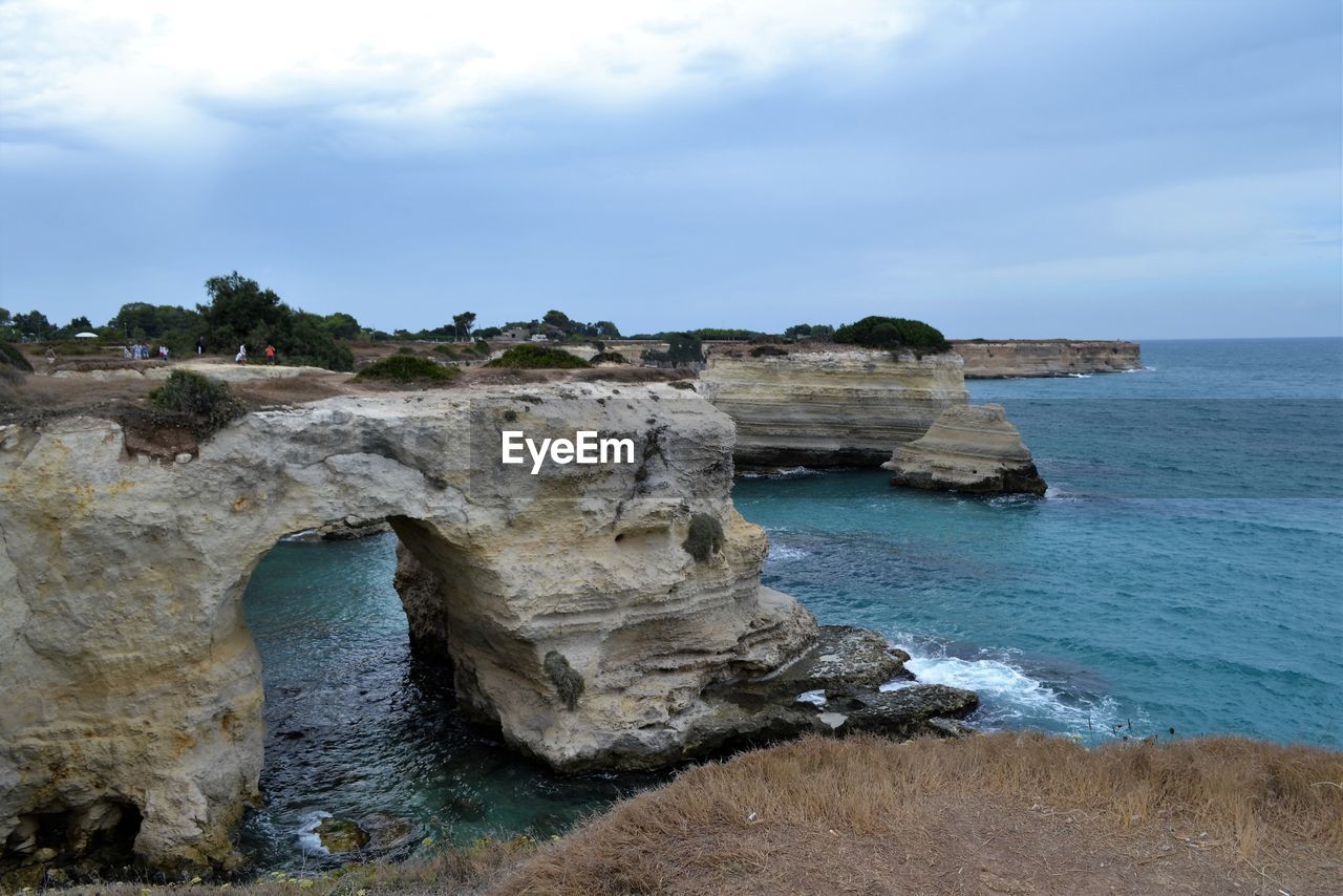 Cliffs in sea against cloudy sky