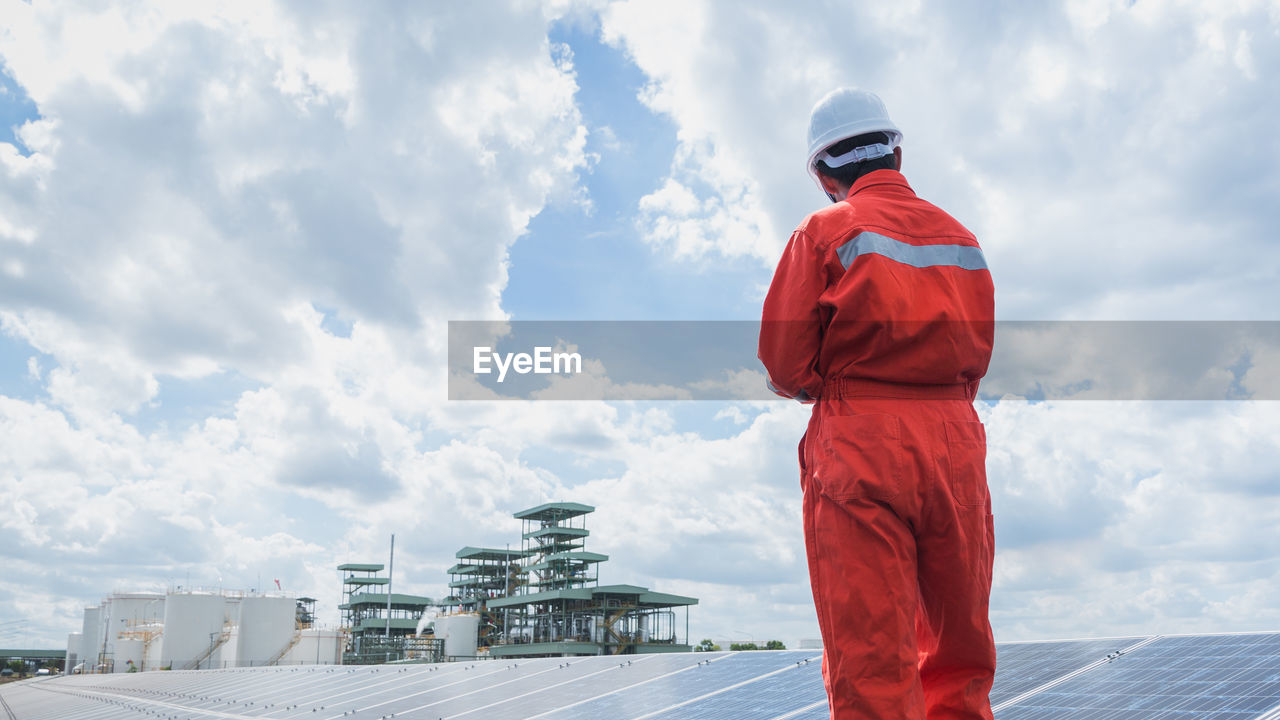 Engineer standing amidst solar panel against cloudy sky