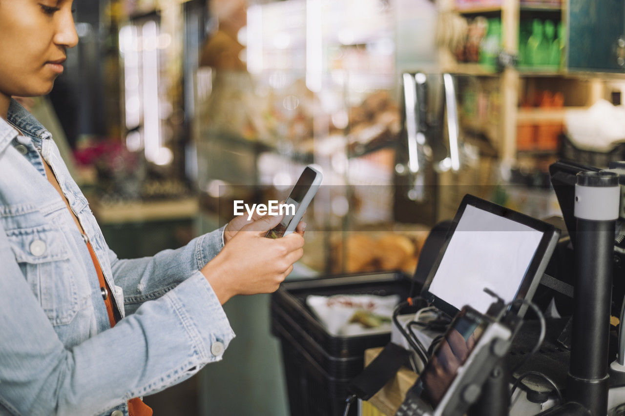 Woman using smart phone while scanning qr code for payment at store checkout