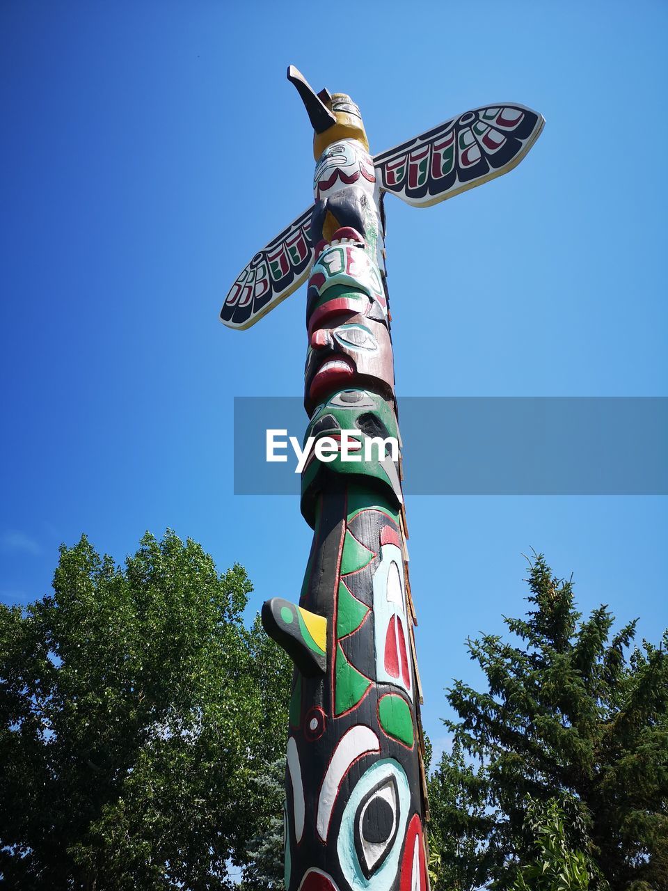 LOW ANGLE VIEW OF STATUE AGAINST TREES AGAINST BLUE SKY