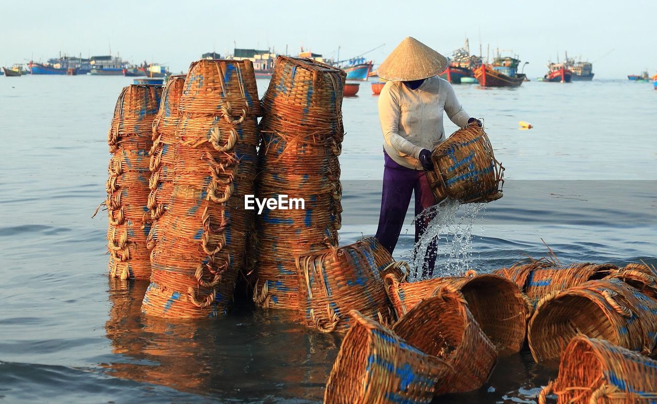 Woman washing old whicker baskets in sea