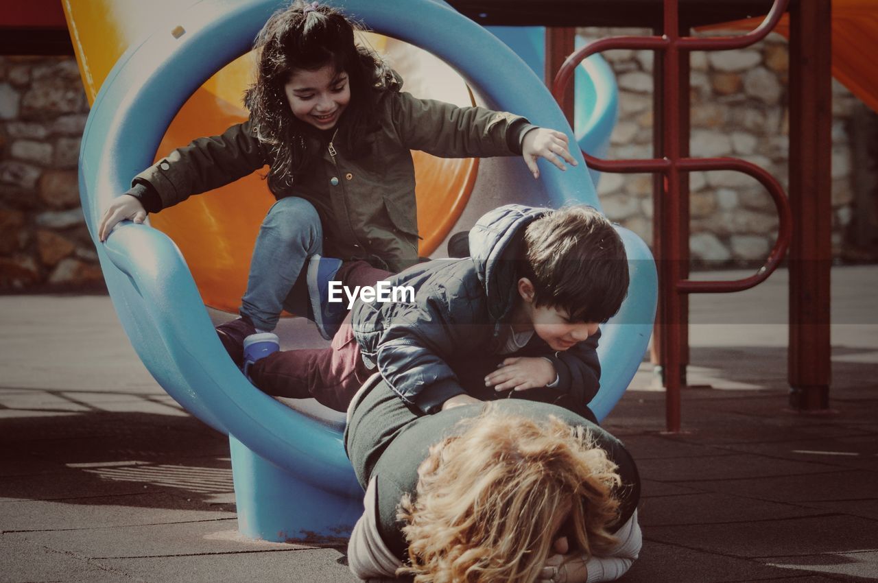 Grandmother with cheerful grandchildren in slide at playground