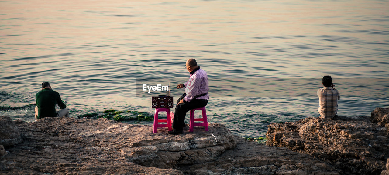 MEN SITTING AT SHORE