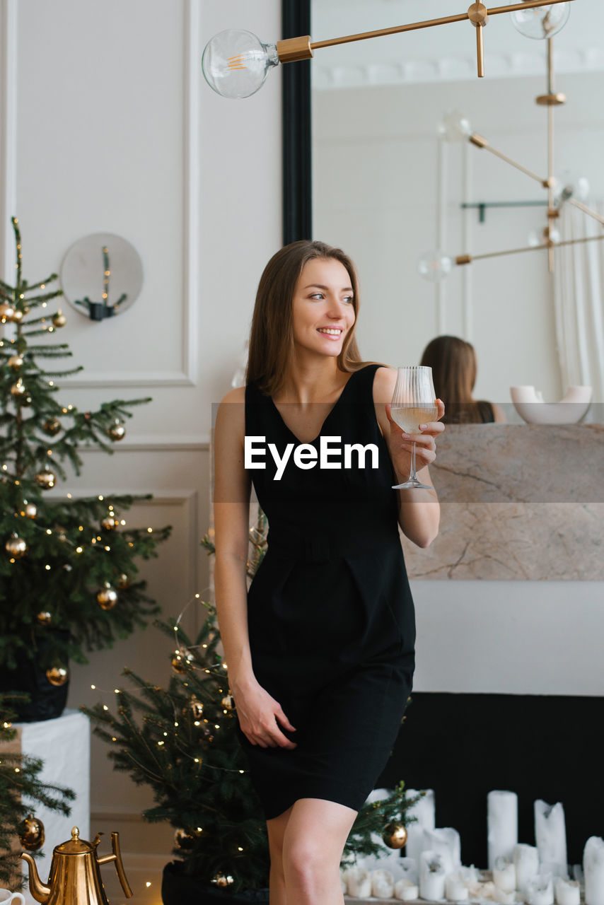 Stylish young woman in a black dress holds a glass of champagne in her hands and celebrates