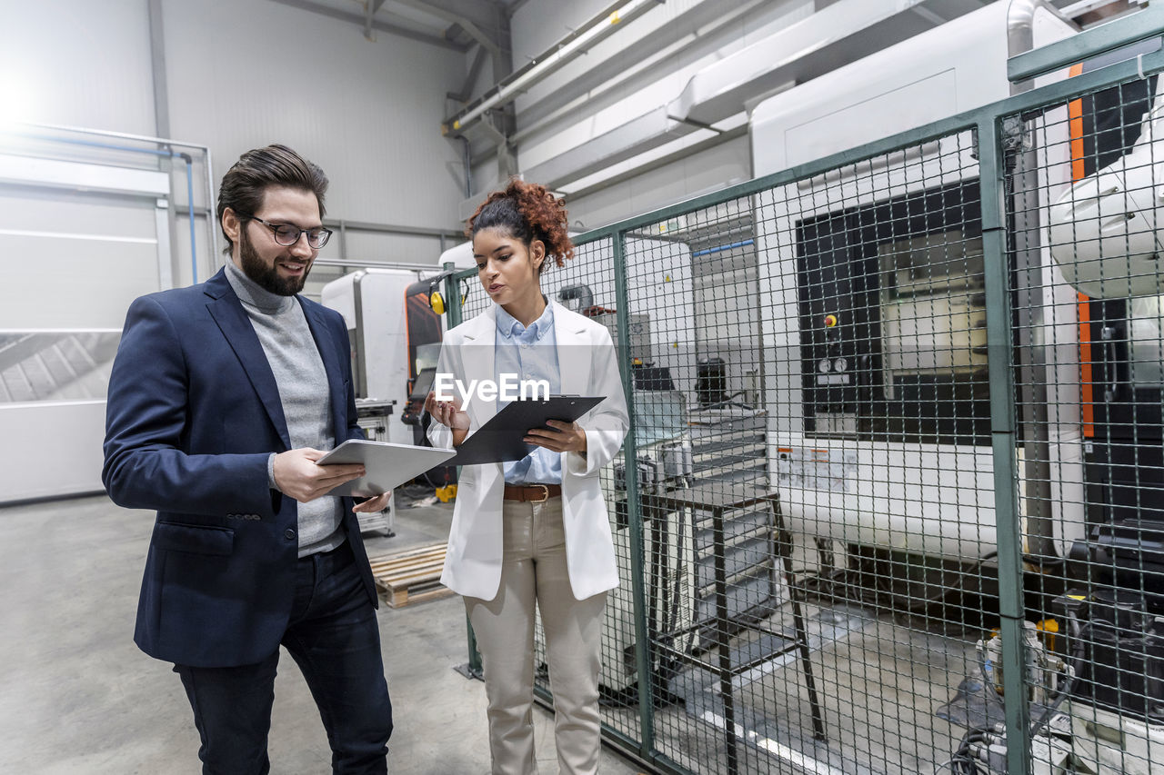 Young engineers discussing over tablet pc in front of machinery