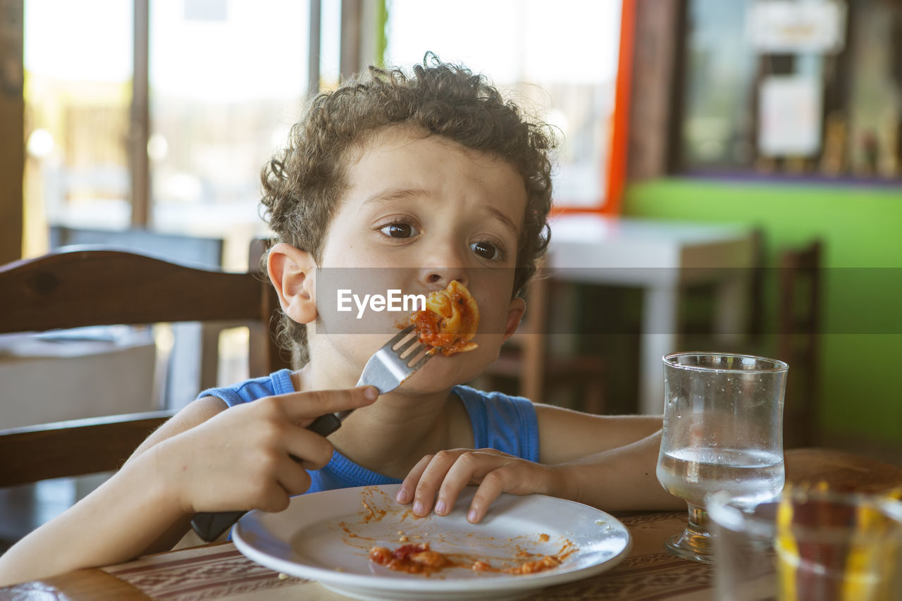 Funny curly-haired boy eating tortellini in restaurant