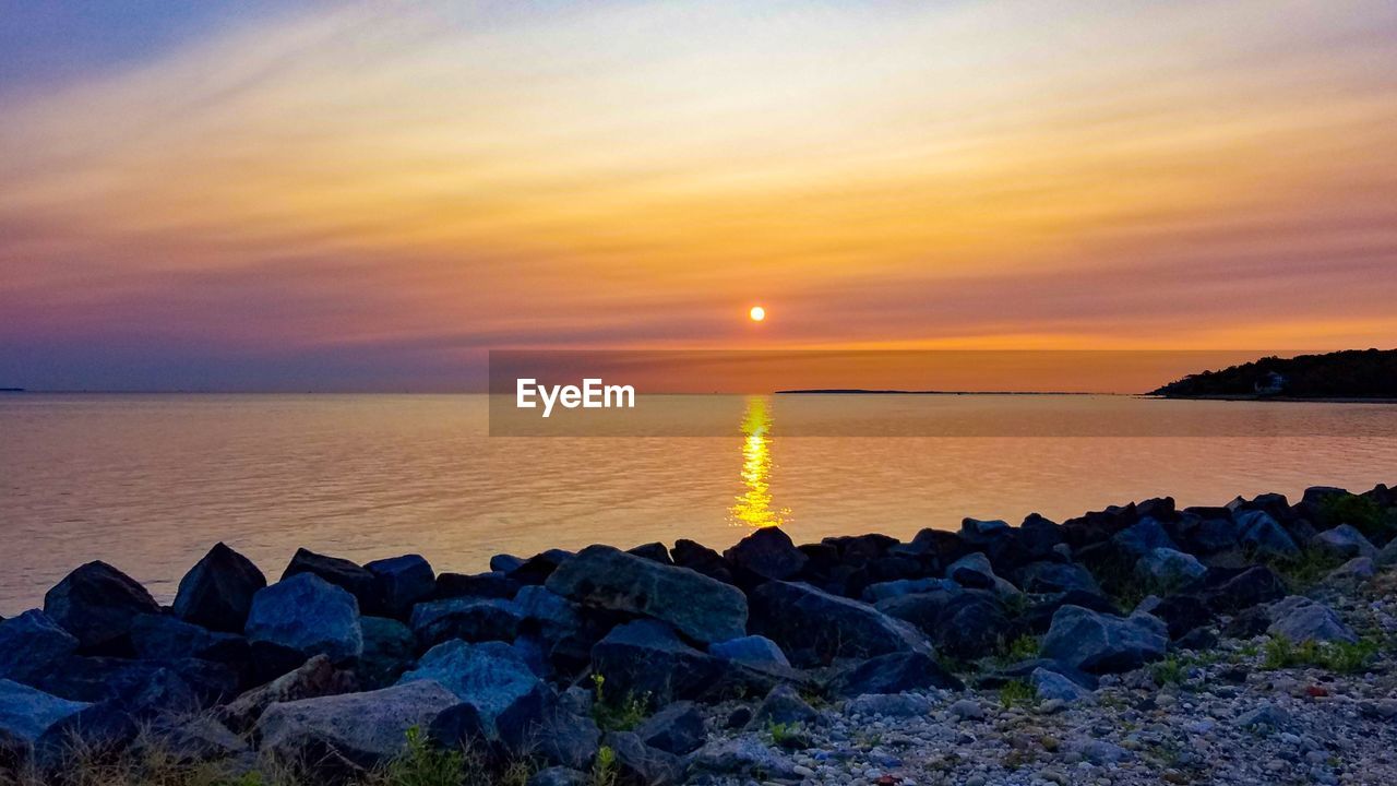 ROCKS BY SEA AGAINST SKY DURING SUNSET