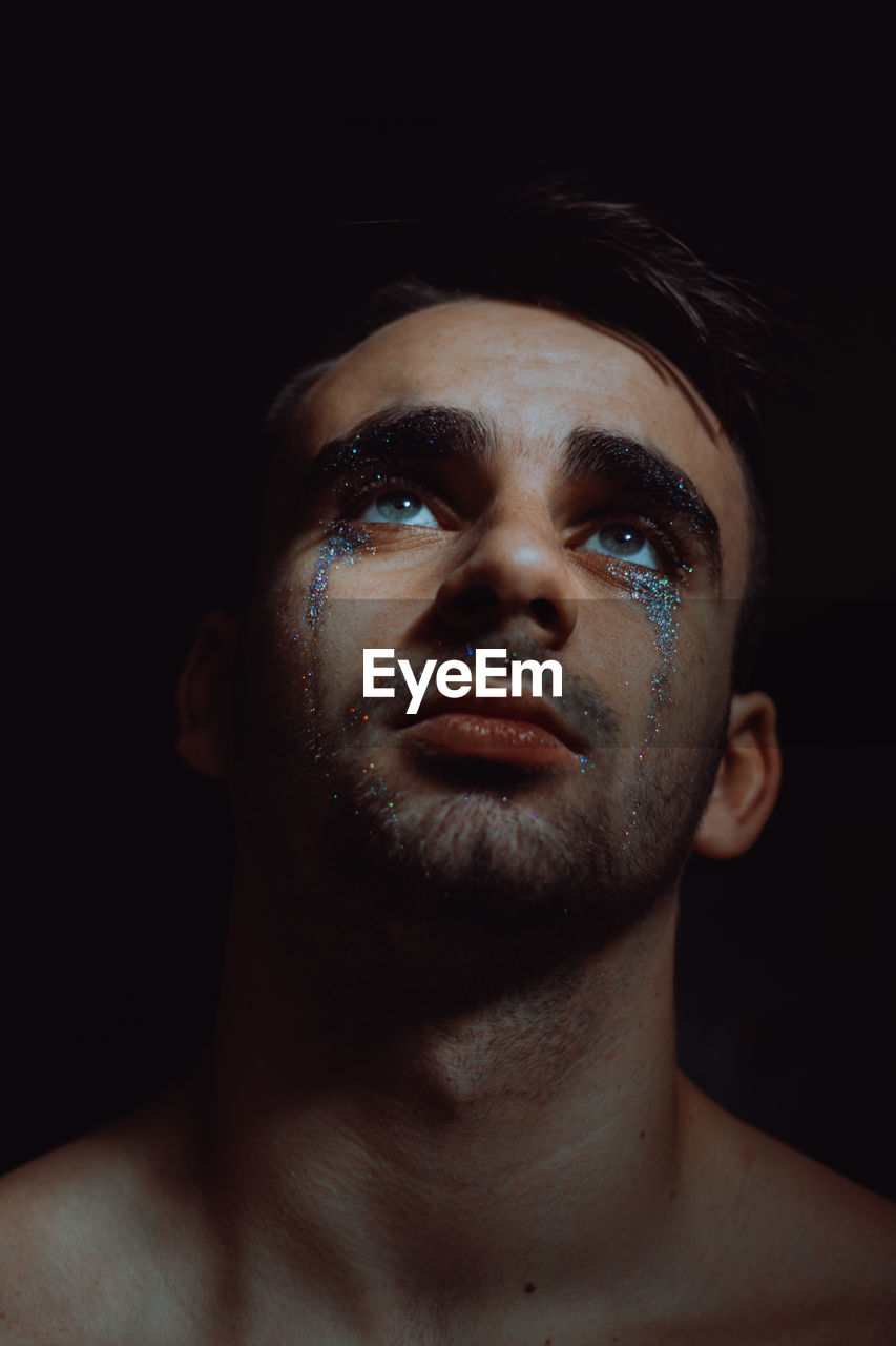 Close-up of man with glitter on face against black background