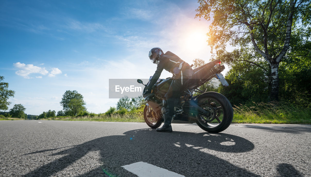Low angle view of man riding motorcycle on road against trees