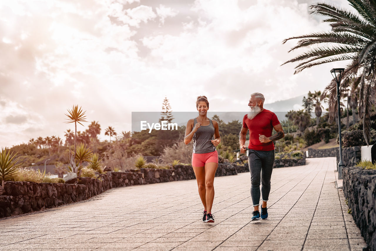 Full length of friends jogging on footpath against sky