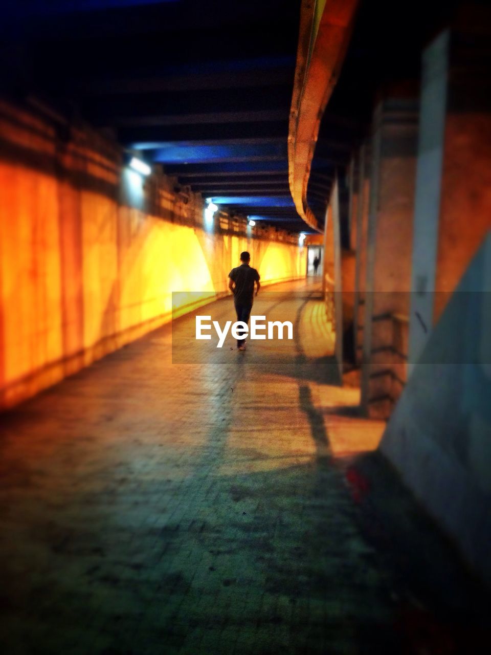 Rear view of man walking in illuminated tunnel