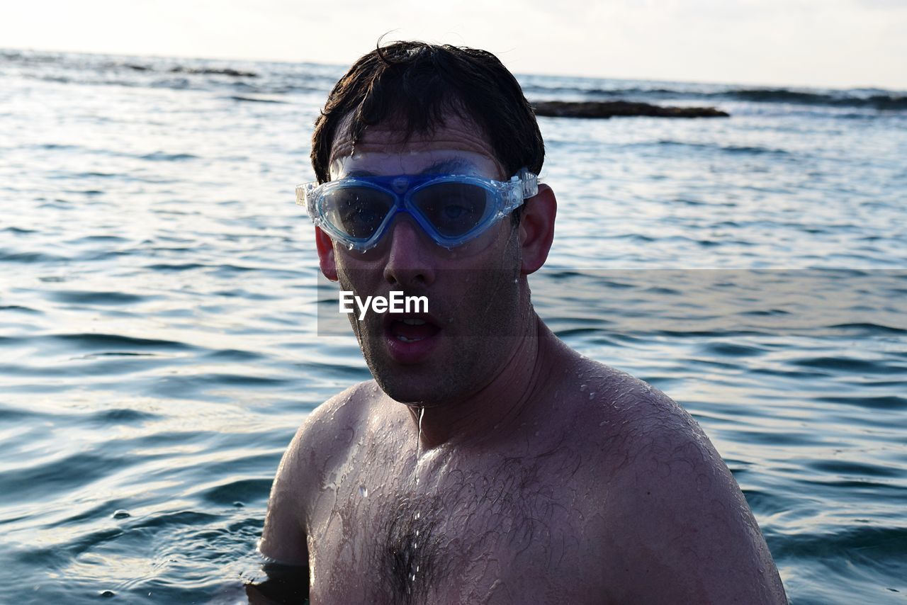 Portrait of shirtless man with swimming goggles in sea