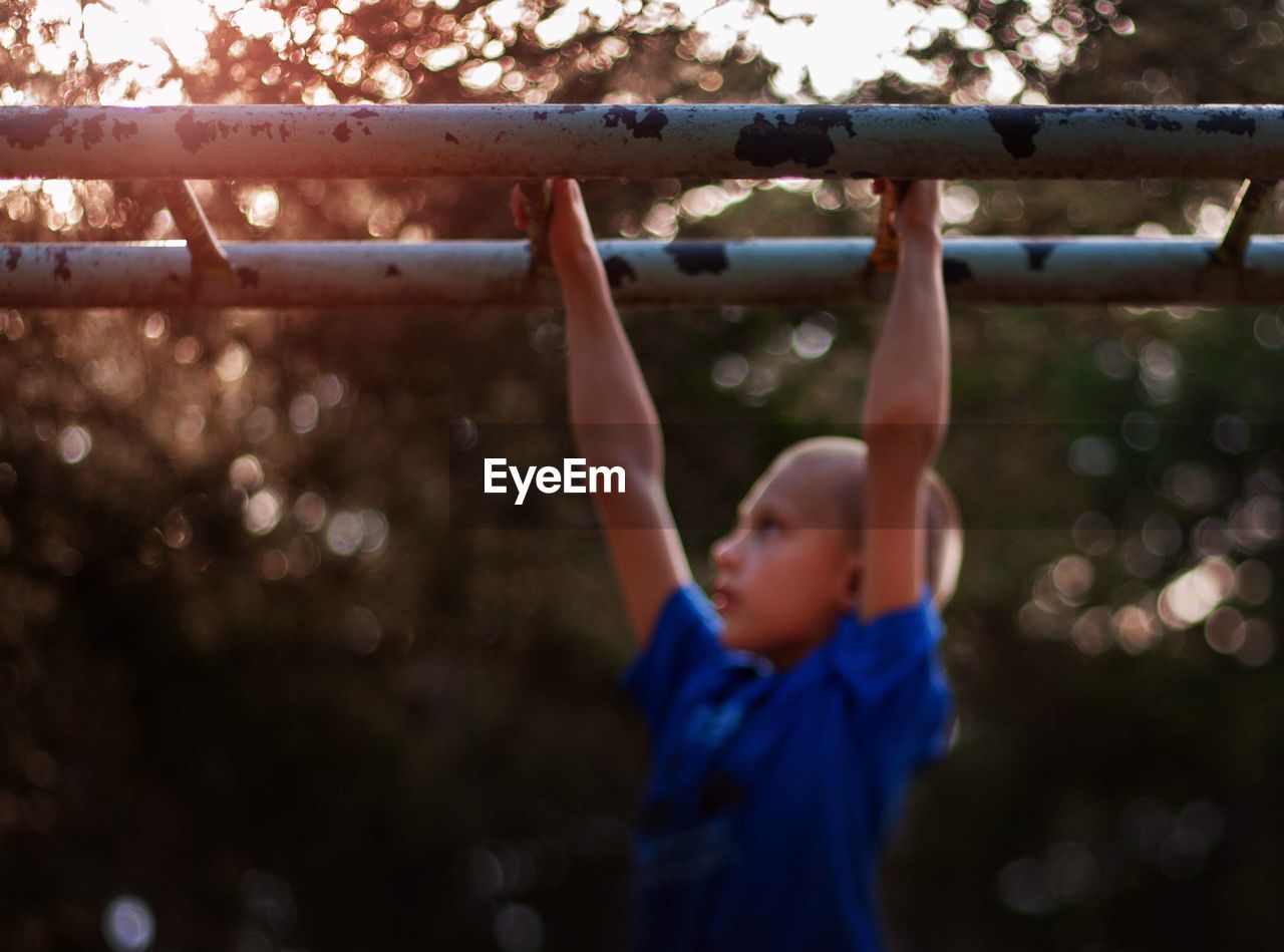 Side view of boy hanging on monkey bars at playground during sunset