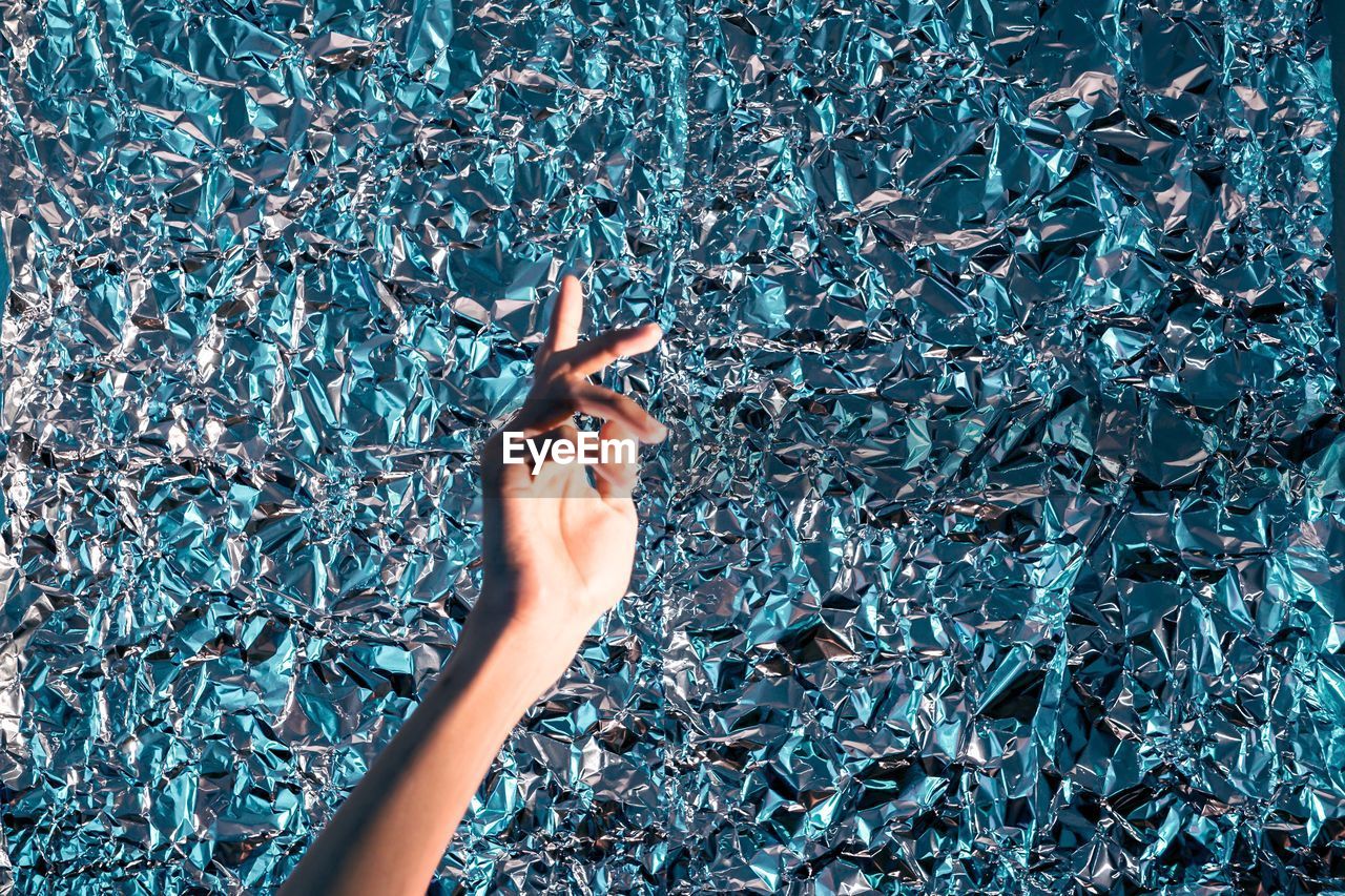 Cropped image of woman hand against foil paper