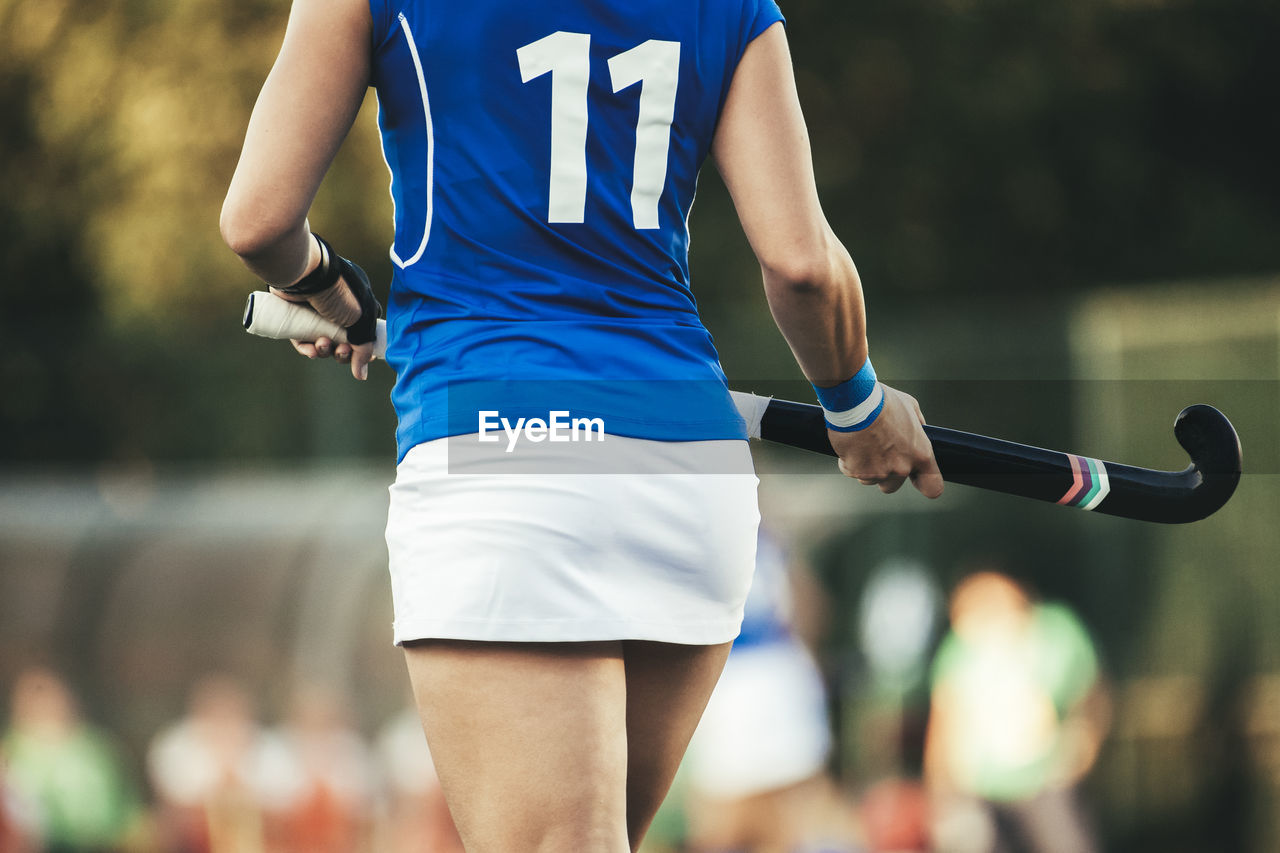 Midsection of hockey player holding bat while walking in stadium