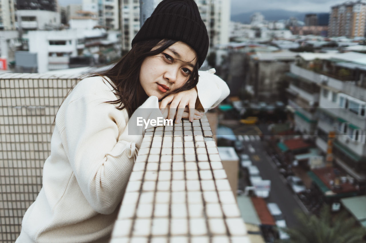 PORTRAIT OF YOUNG WOMAN AGAINST CITYSCAPE