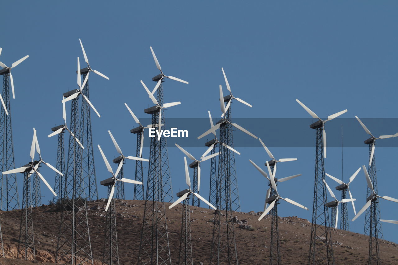 Windmills on landscape against clear blue sky