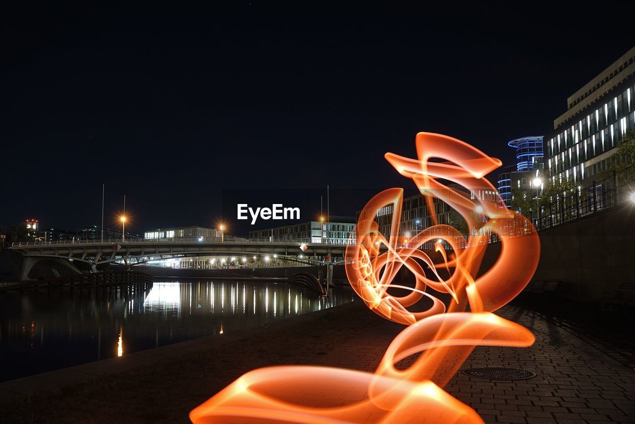 Light painting by river against sky in city at night