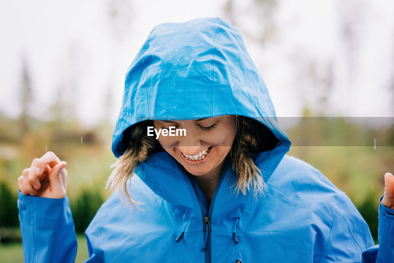 Woman stood in the rain smiling outside in a raincoat