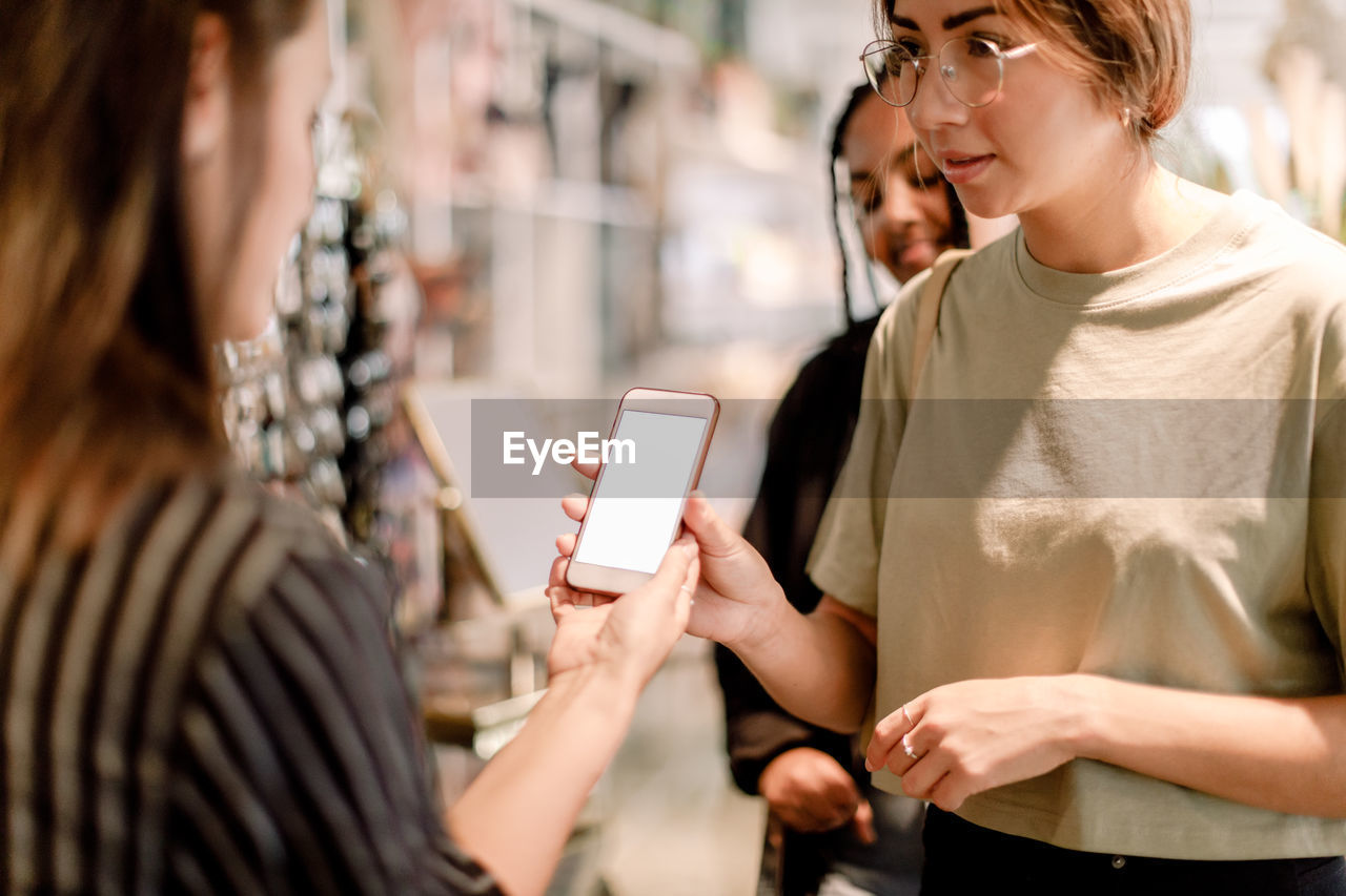 Woman showing phone to saleswoman at fashion store