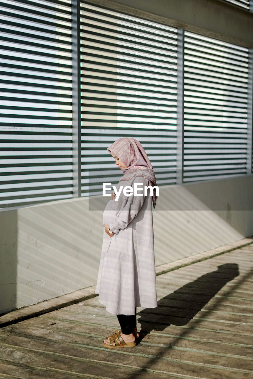 REAR VIEW OF WOMAN STANDING AGAINST FOOTPATH