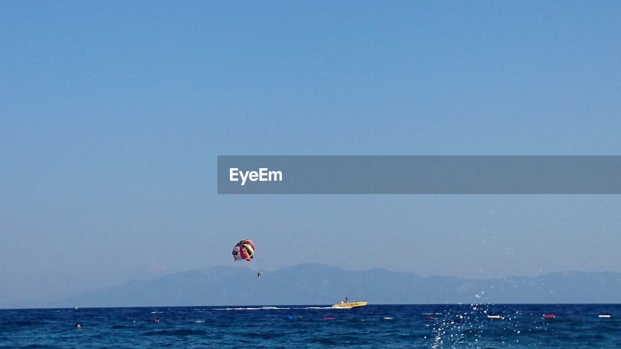 PERSON PARAGLIDING IN SEA AGAINST CLEAR SKY