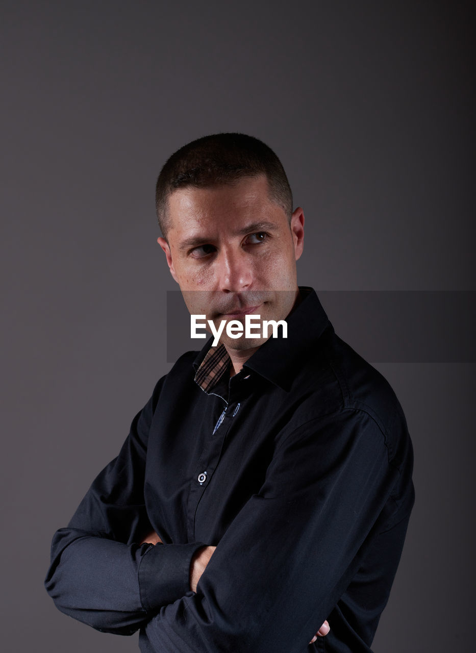 studio shot, one person, portrait, adult, men, looking at camera, indoors, gray background, waist up, gray, serious, black, formal wear, person, business, arms crossed, outerwear, emotion, mature adult, clothing, front view, shaved head, standing, tuxedo, copy space, businessman, cut out