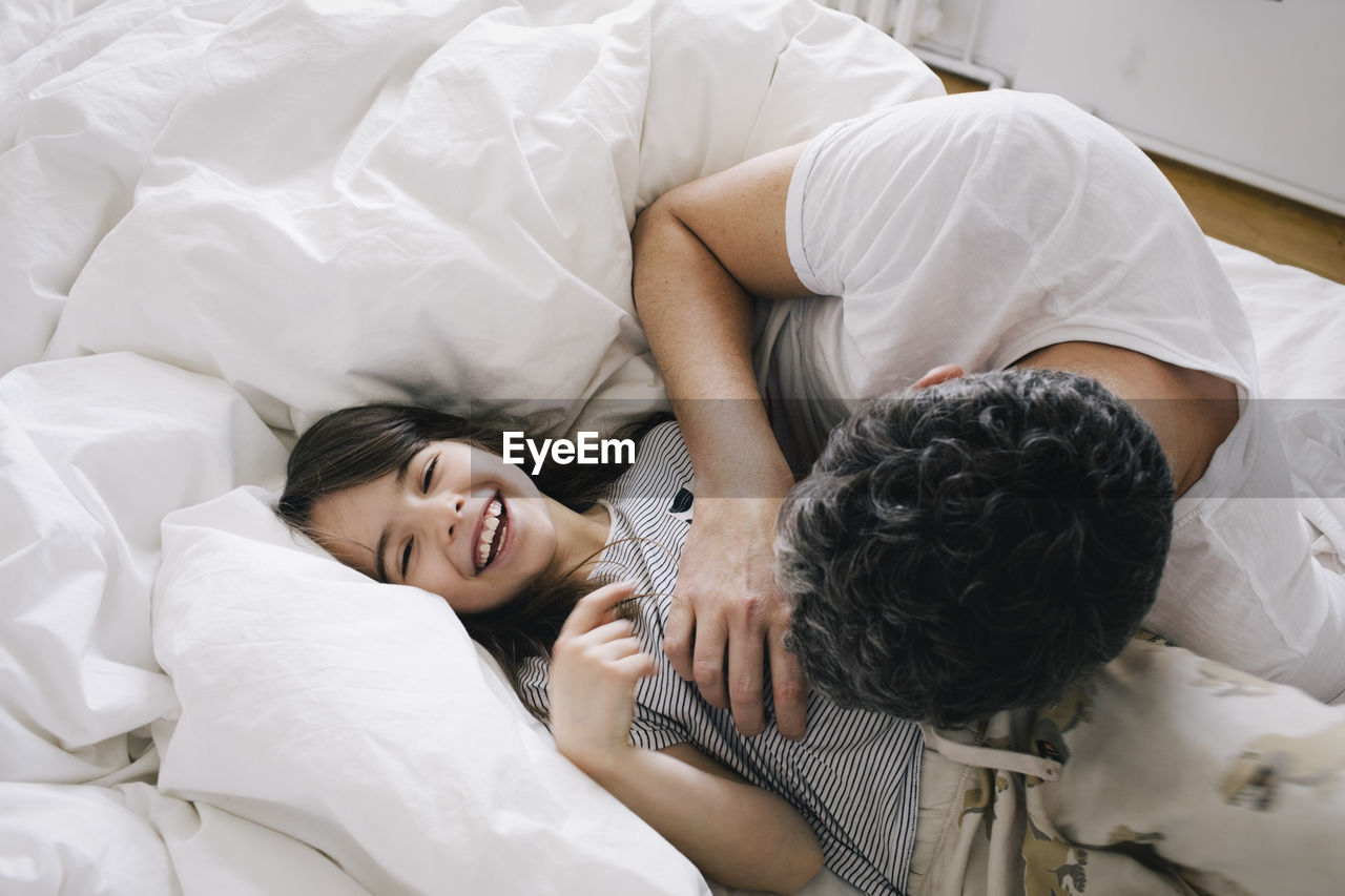 Playful father playing with daughter lying on bed at home