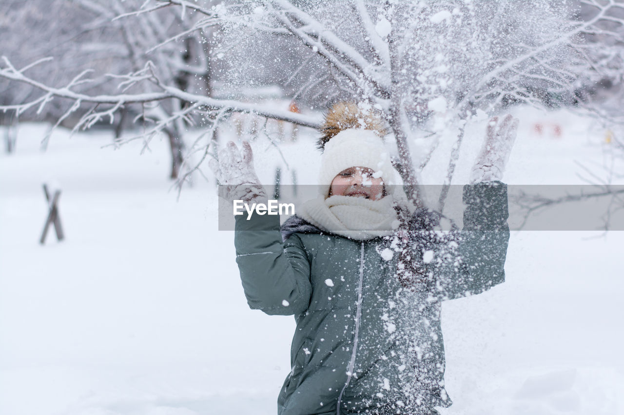A girl in warm clothes throws snow in front of her in a winter park. winter lifestyle portrait