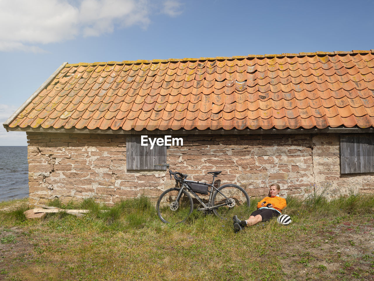 Cyclist relaxing near stone house at sea