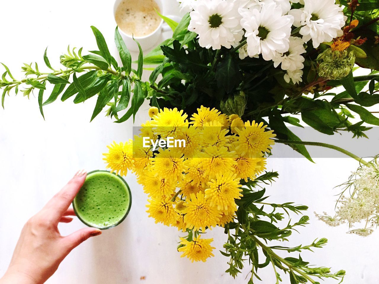 Cropped hand holding avocado smoothie by flowers on table