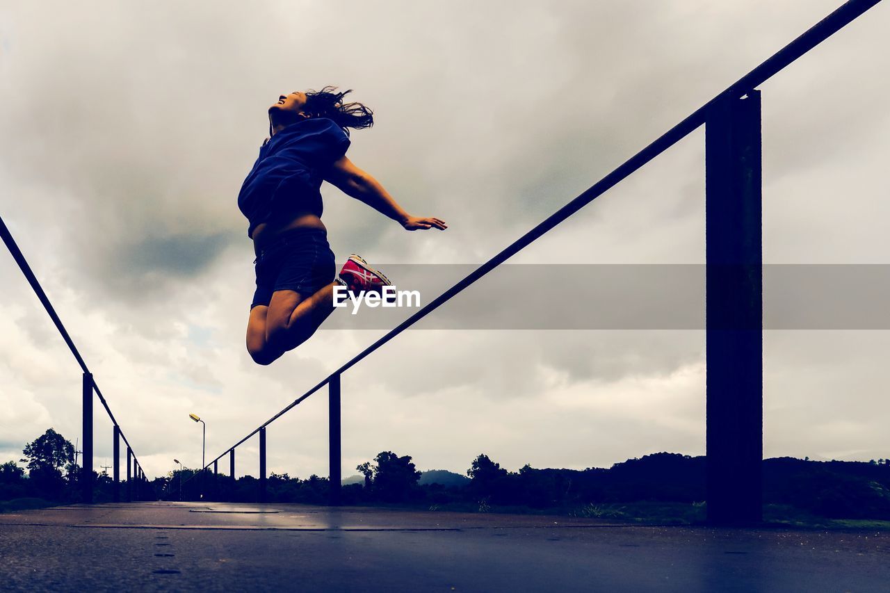 SIDE VIEW OF MAN JUMPING AGAINST CLOUDY SKY