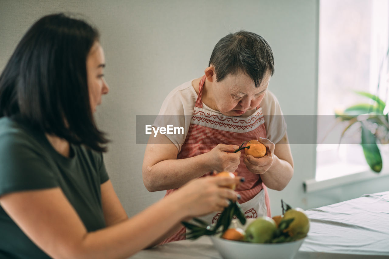 Elderly woman with down syndrome finds joy and independence in peeling mandarin with a teacher