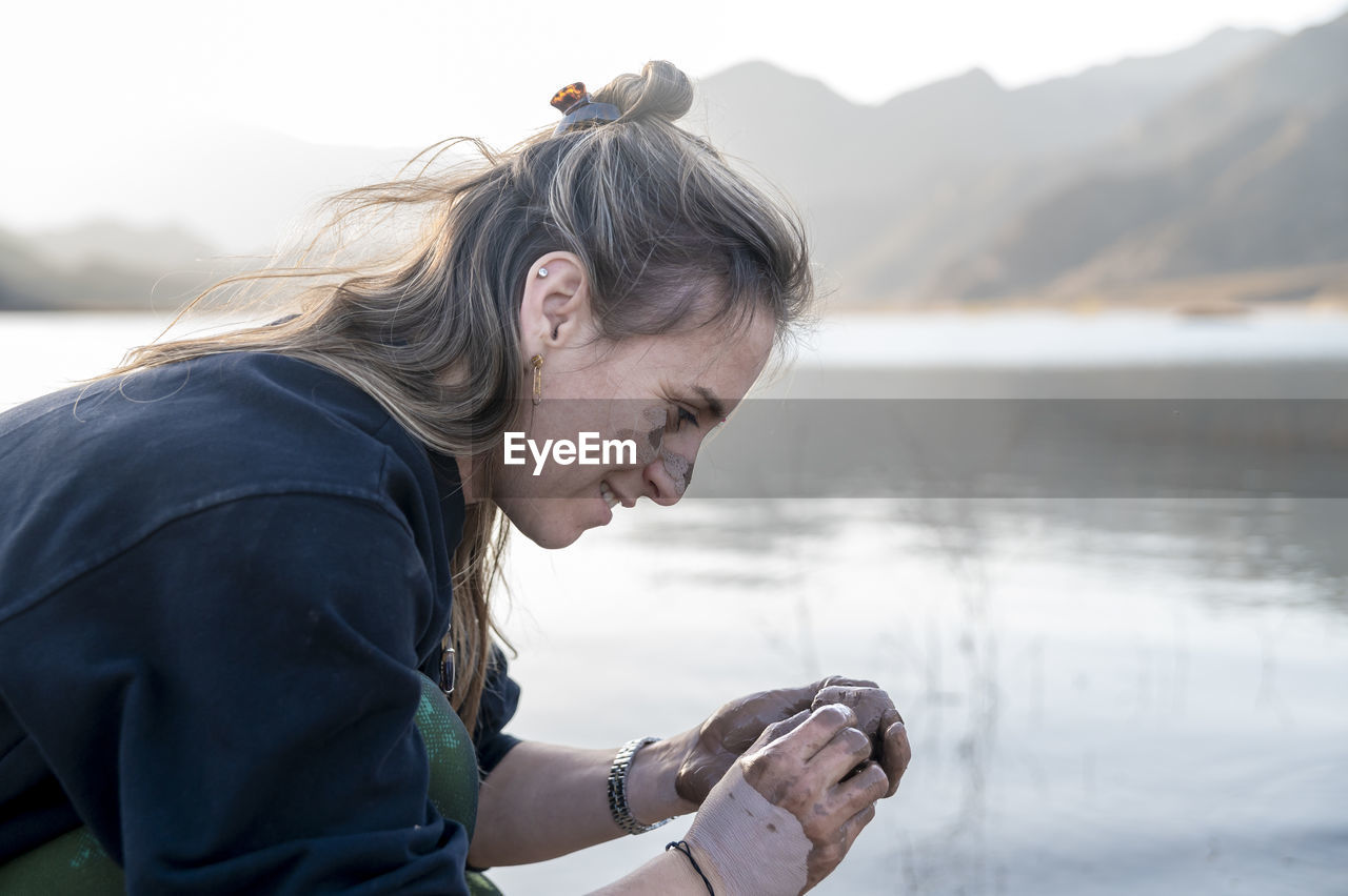 Woman putting mud on hands and face while enjoying outdoors in nature.