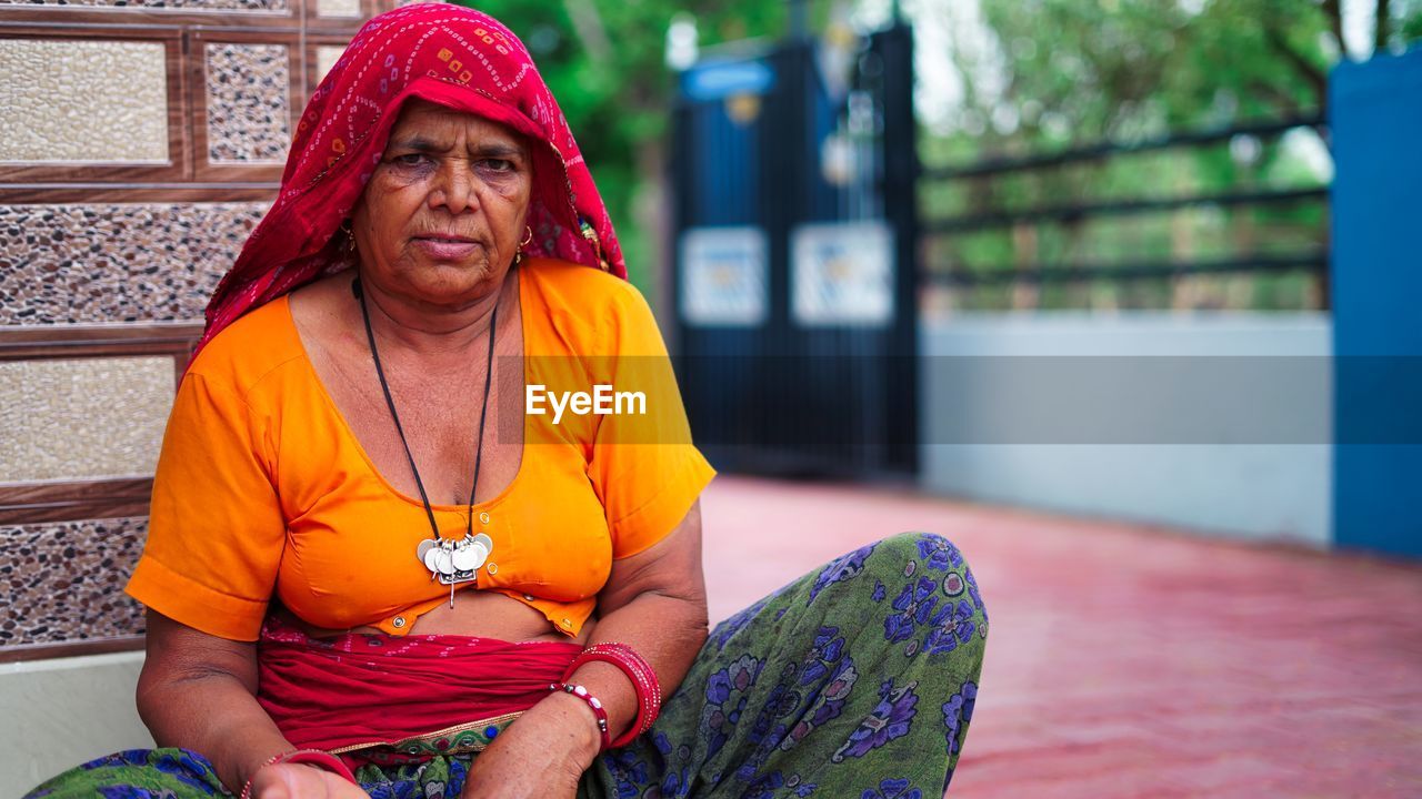 Portrait of indian senior woman sitting near main entrance and looking at camera.