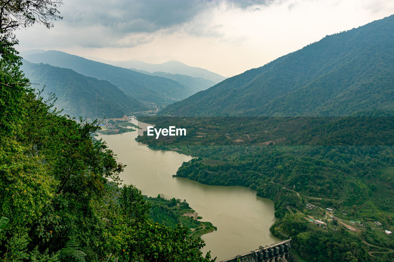 Mountain valley with cloudy sky and river leading at morning from flat angle