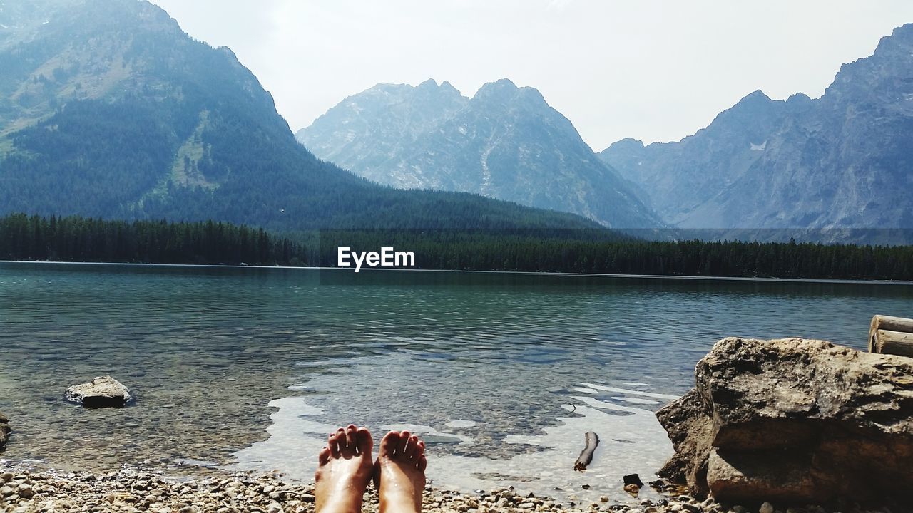 Low section of woman relaxing by leigh lake against teton range