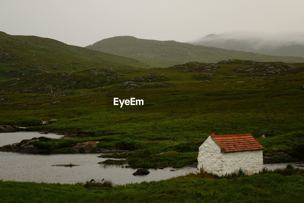 House on riverbank by mountains against sky at dusk