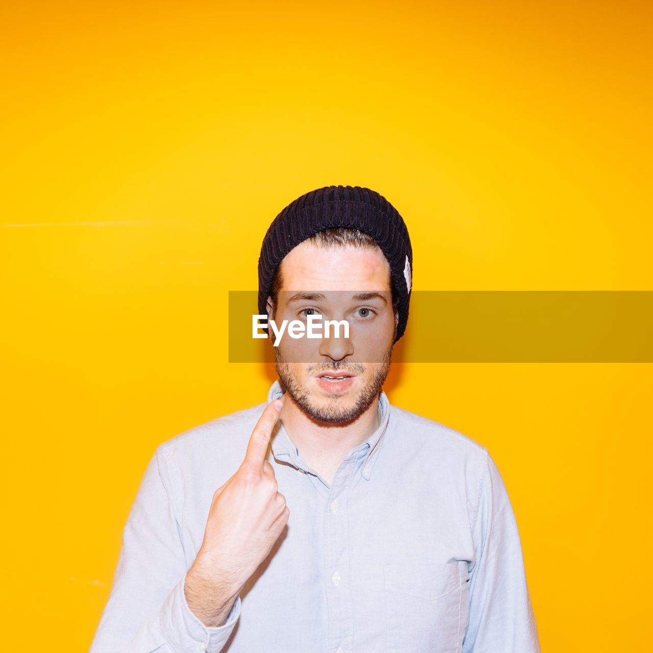 Portrait of young man showing index finger against yellow background