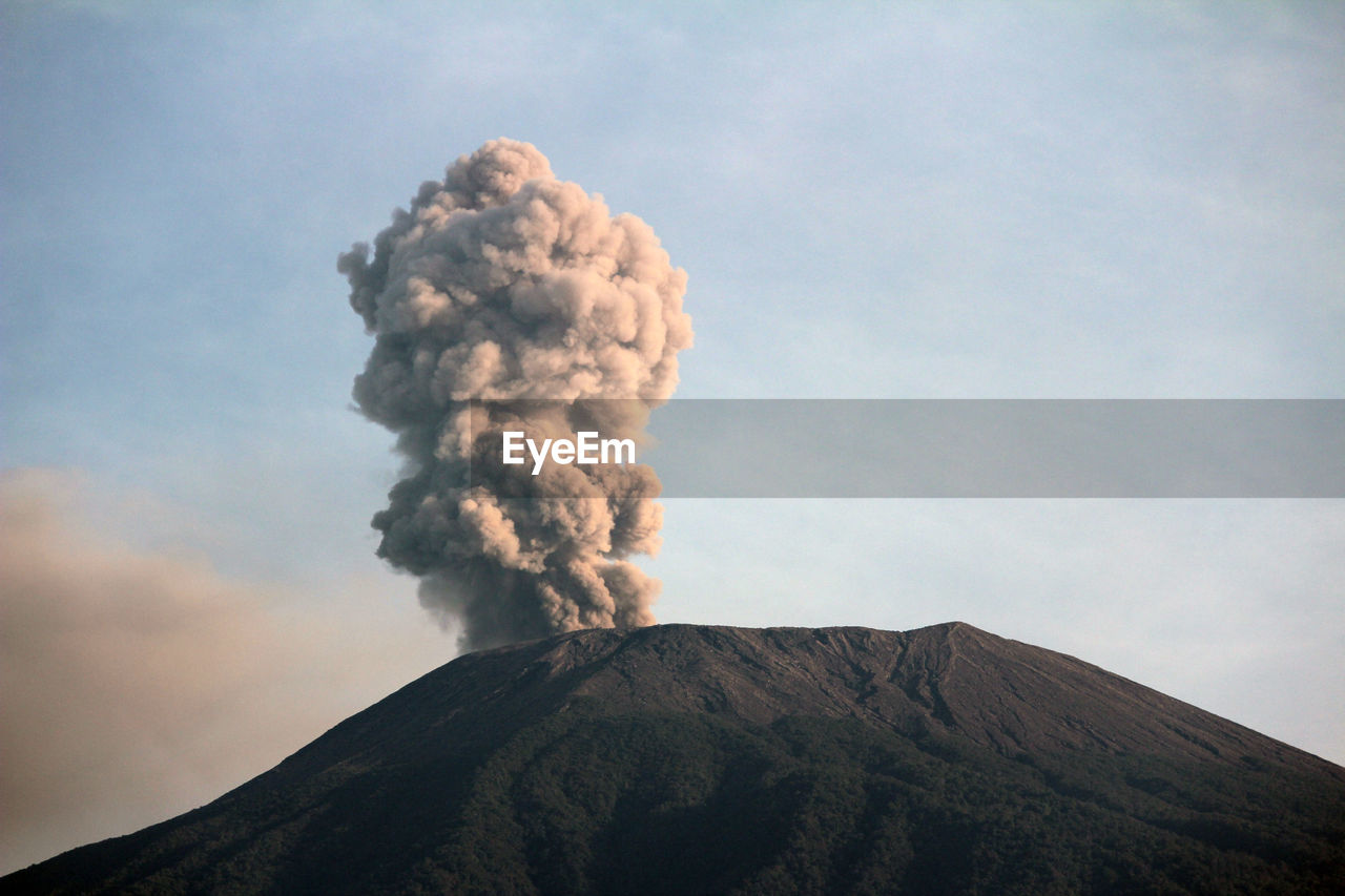 Smoke emitting from volcanic mountain against sky - slamet mount