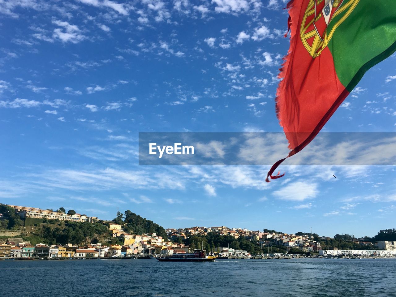 Scenic view of a portuguese flag at the back of a boat with blue sky and a small village in the back
