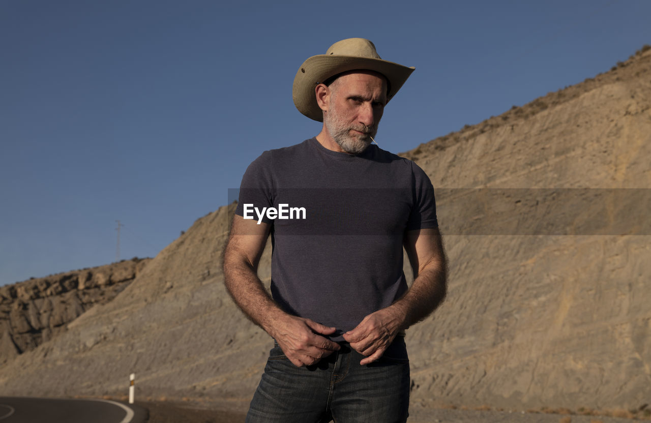 Adult man in cowboy on roadside on desert against mountain. almeria, spain