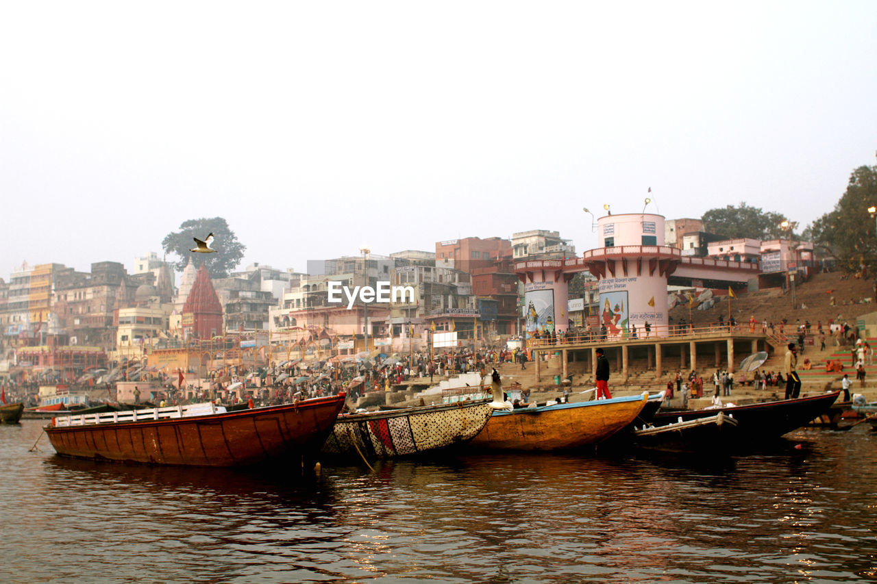 Sailboats moored in river by buildings against clear sky