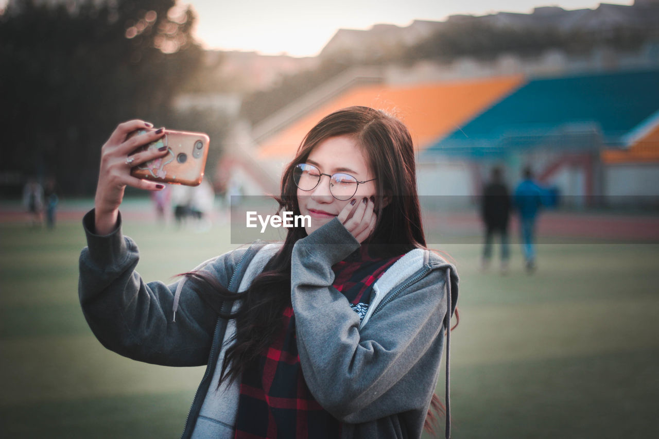 Smiling young woman taking selfie while standing outdoors