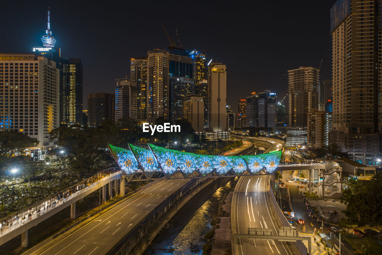 HIGH ANGLE VIEW OF LIGHT TRAILS ON STREET AMIDST BUILDINGS AT NIGHT