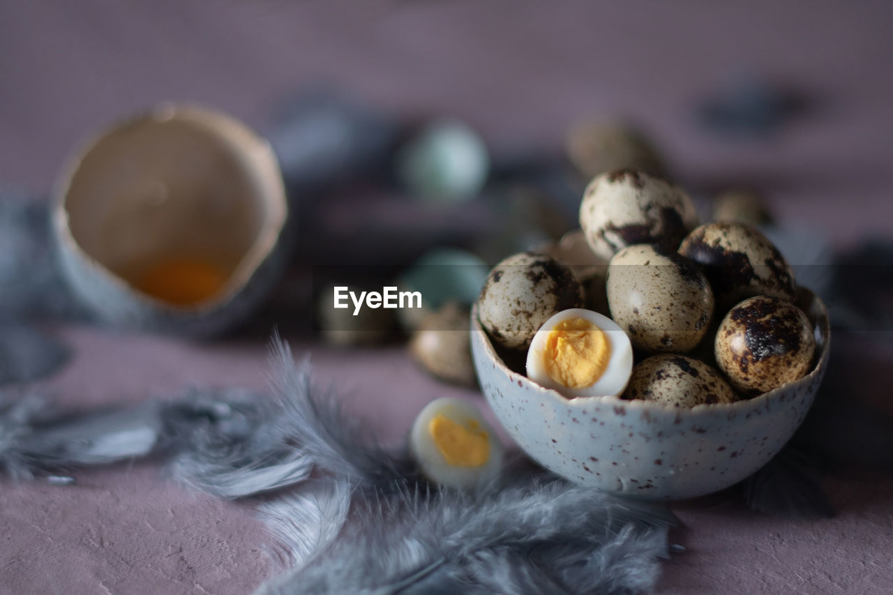 Quail eggs in ceramic vases, gray feathers on the table, easter still life,