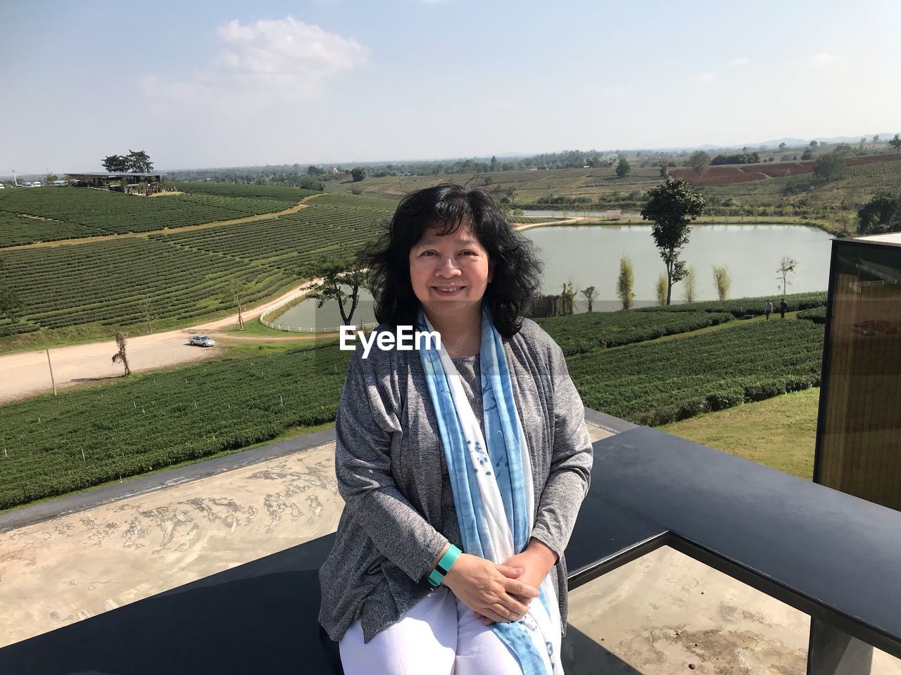 Portrait of smiling woman sitting on bench against landscape and sky