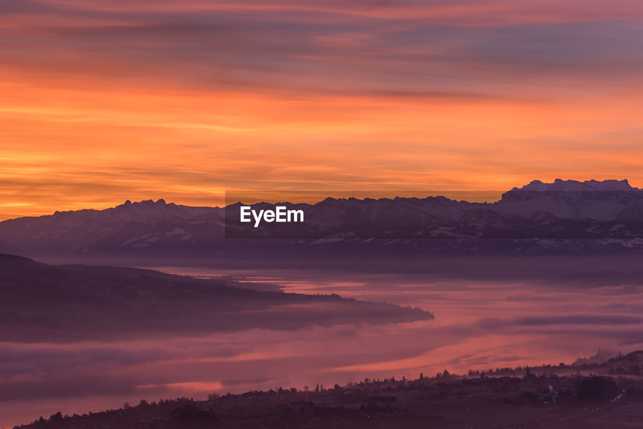 Scenic view of lake zurich and mountains against orange sky