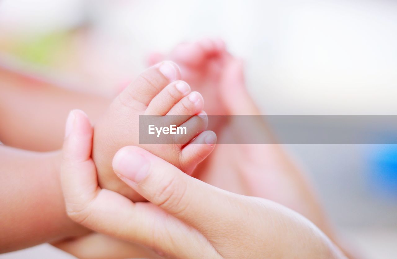 Cropped hands of woman holding baby feet at home